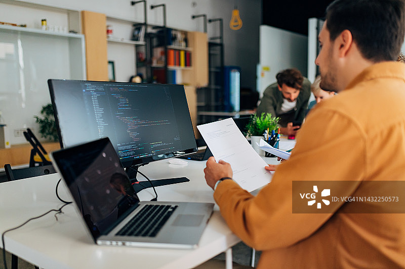 专注的男人学习编写程序，背景中可以看到他的同事图片素材