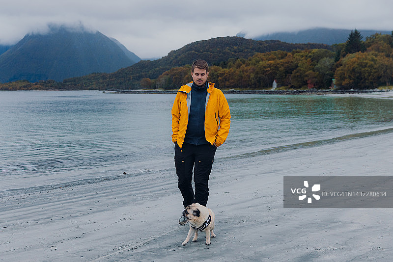 男子与狗在挪威海边欣赏秋景山色图片素材