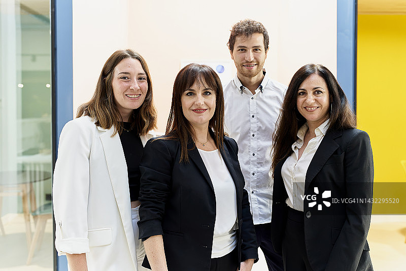 三名女子和一名男子微笑地看着玻璃窗的左前方和背景中的墙壁图片素材