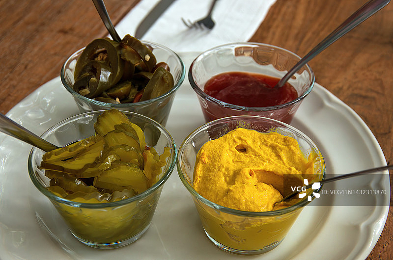 小玻璃碗中的汉堡调味品：腌墨西哥辣椒片、番茄酱、美式芥末和莳萝腌黄瓜片图片素材