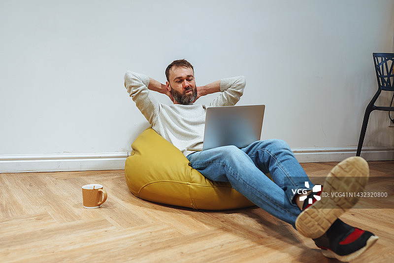 自由职业者在阁楼房间的地板上的豆袋里喝着咖啡放松图片素材
