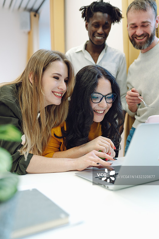 科技爱好者和技术迷喜欢新笔记本电脑。同事们在办公室里玩得开心，看着笔记本电脑。图片素材