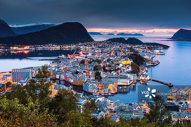 挪威奥勒松市的夜景照片。美丽的峡湾夜景，斯堪的纳维亚。水中倒映着灯光，群山笼罩在暮色中图片素材