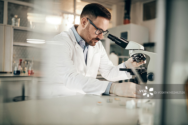 年轻男化学家在实验室显微镜下调整样品图片素材