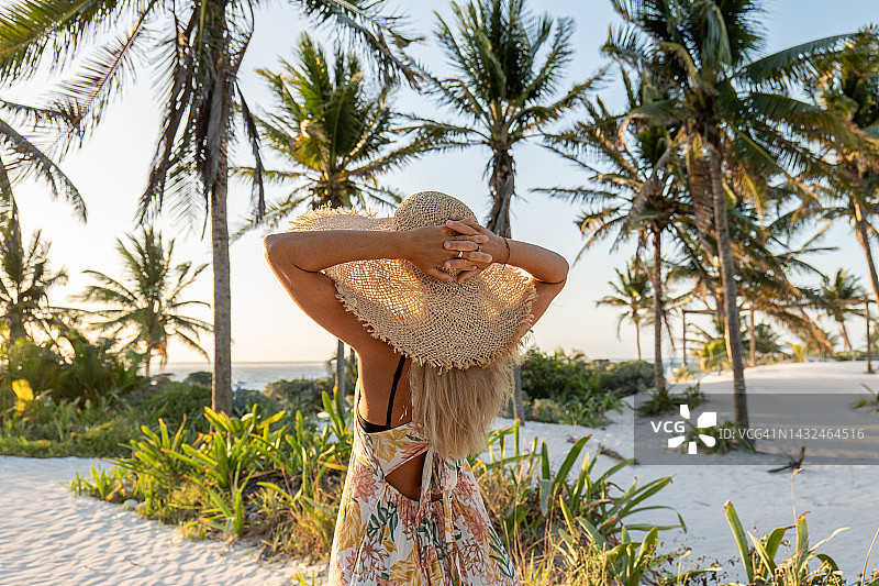 年轻女子在日落时走向热带海滩图片素材