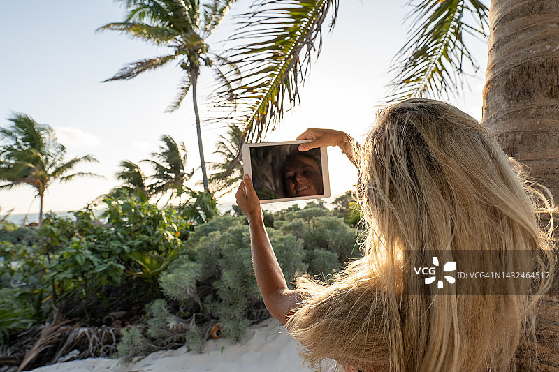 美丽年轻女人在热带沙滩日落时使用平板电脑图片素材