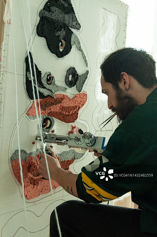 在工作室使用簇绒枪和腈纶纤维制作手工地毯的30岁白胡子男人图片素材