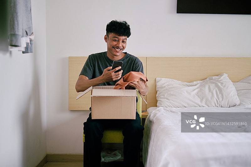 年轻男子在手机上发短信时打开包裹图片素材