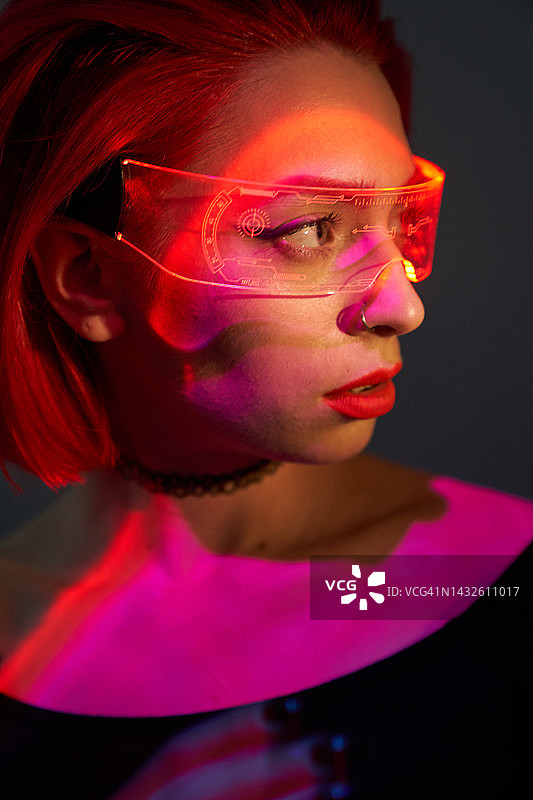 戴红色头发和未来主义眼镜的美丽年轻女人，红光，数字时代智能眼镜与霓虹灯，未来概念、外星智能、数字技术和黑客攻击、电脑游戏、虚拟现实图片素材