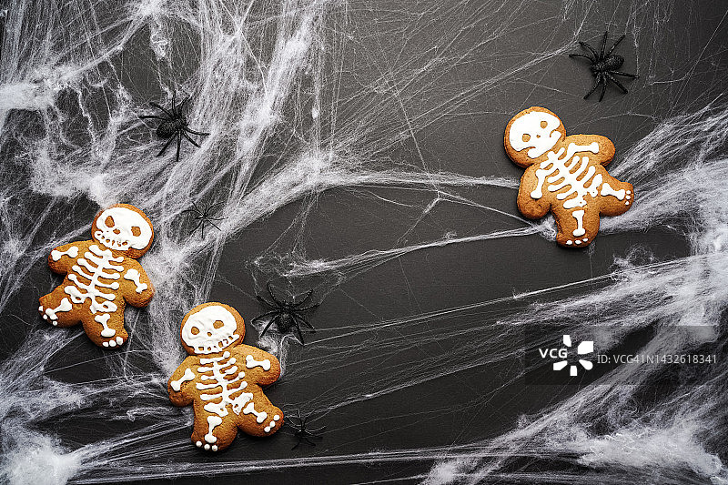 黑色万圣节背景，姜饼骷髅蛋糕、闪光蜘蛛和白色蜘蛛网图片素材