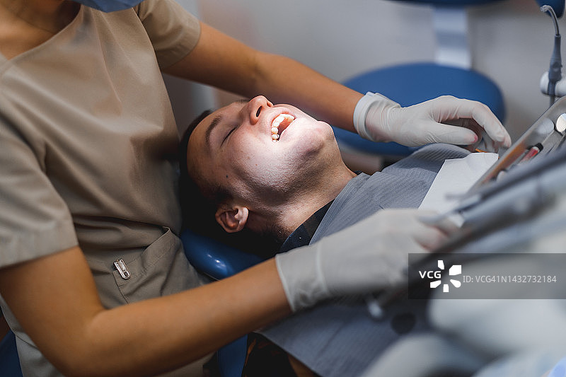 牙医为男士在现代诊所进行治疗的合影。牙科诊所的医疗概念摄影，医生在诊所为病人工作。图片素材