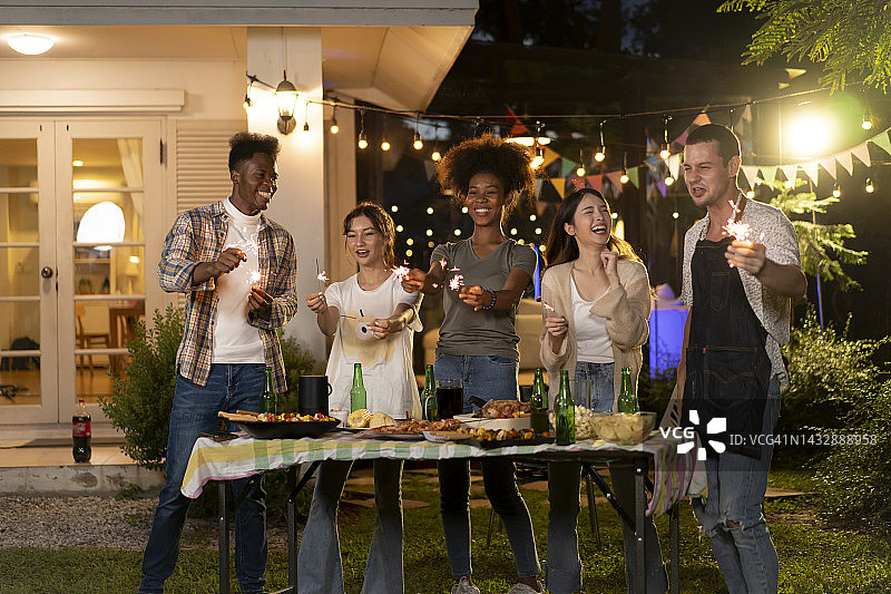 在灯光照亮的后院举办晚宴的多民族朋友们图片素材