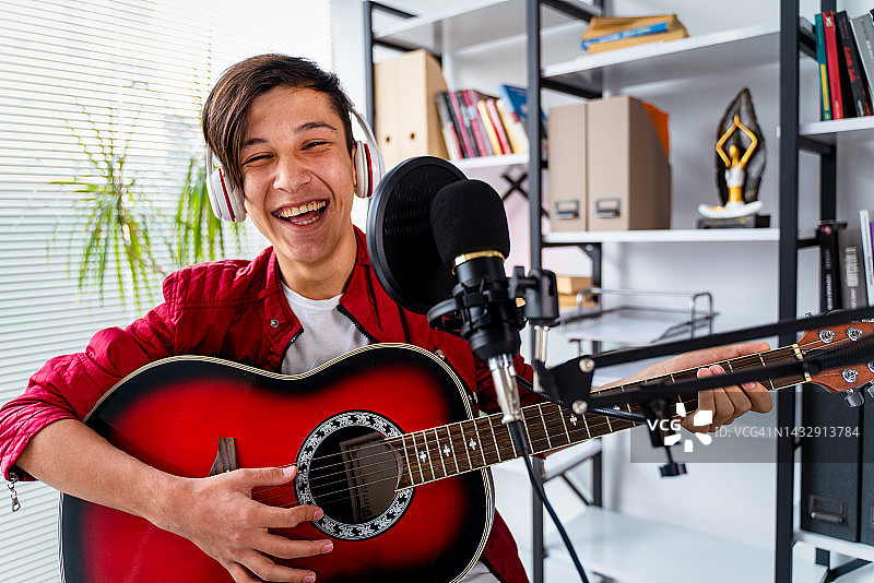 青少年男孩戴着耳机，在麦克风前弹吉他录歌图片素材