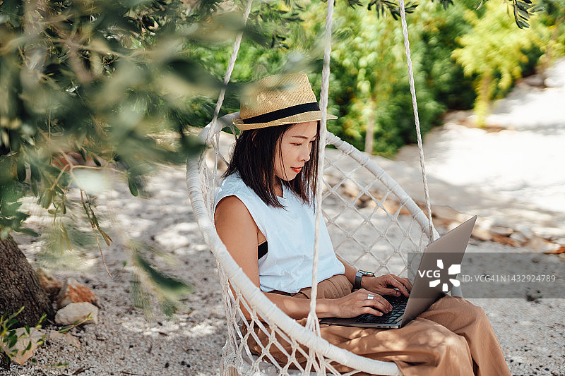年轻女人在花园秋千椅上使用笔记本电脑图片素材