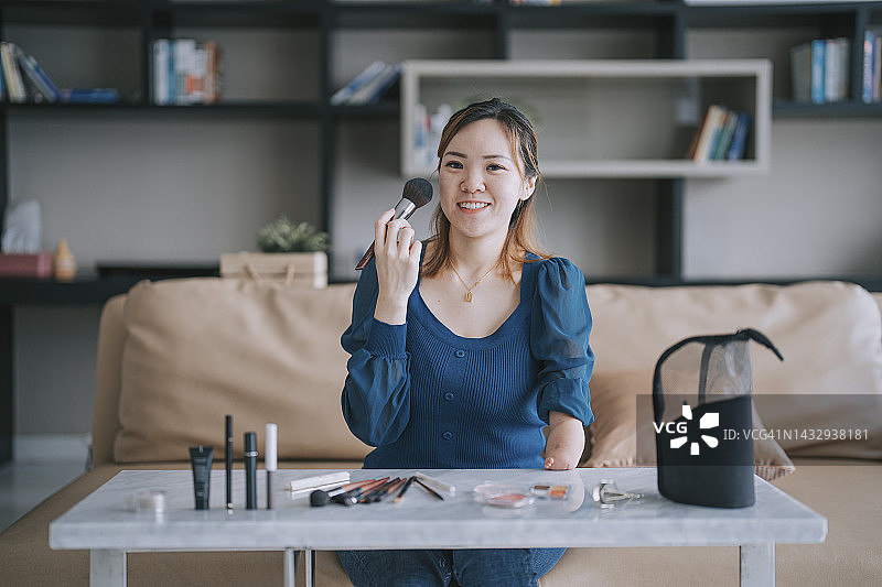 中国残疾女视频博主看着镜头微笑，拿着化妆刷直播图片素材