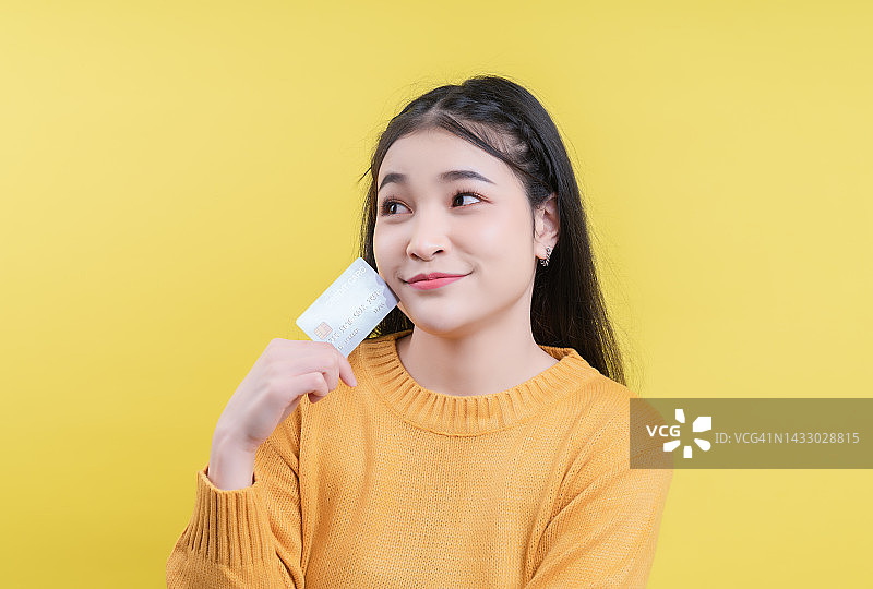 穿着黄色衣服，拿着信用卡，看着空白区域的沉思的年轻女子图片素材