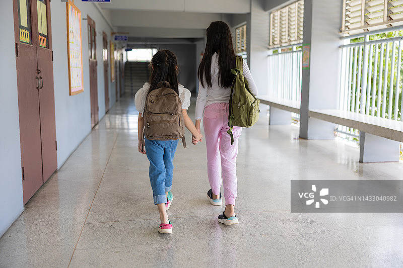 两名背着书包的亚洲小学生走在教学楼的走廊上图片素材