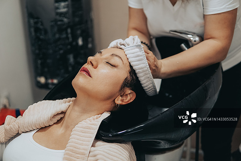 在美发沙龙里，理发师用毛巾为女人洗头和吹干头发图片素材