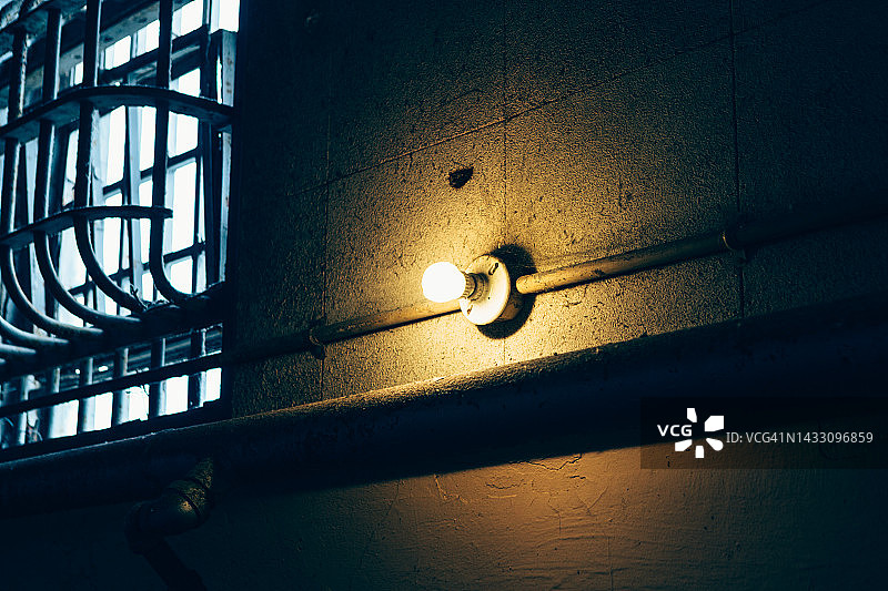 昏暗房间里带铁栅栏窗户的灯泡图片素材