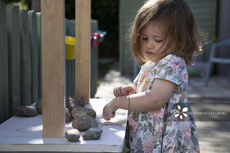 幼儿在夏天的户外桌子上玩绳子和石头图片素材