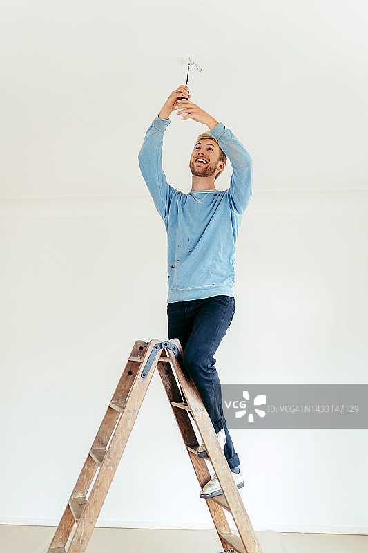 年轻男人在家站在梯子上更换灯泡图片素材