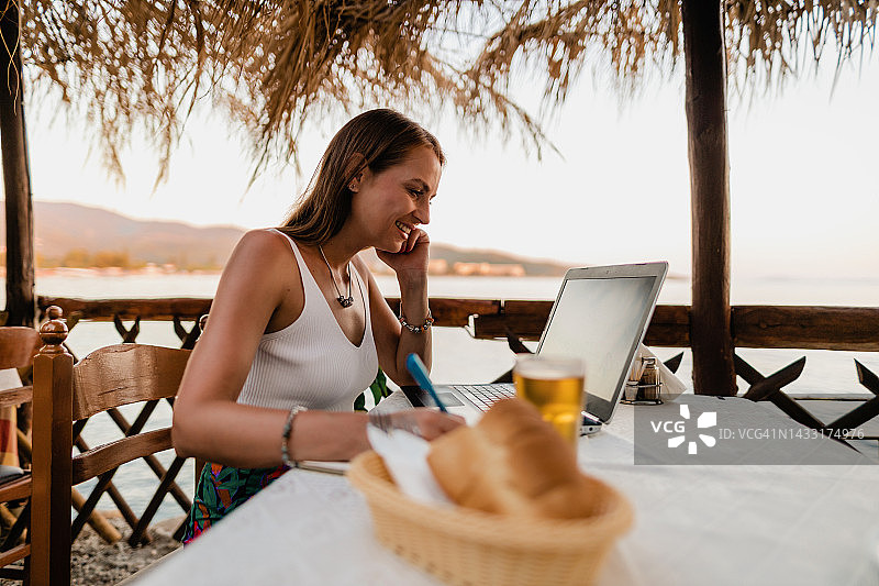 在希腊海边餐厅学习的年轻女人图片素材
