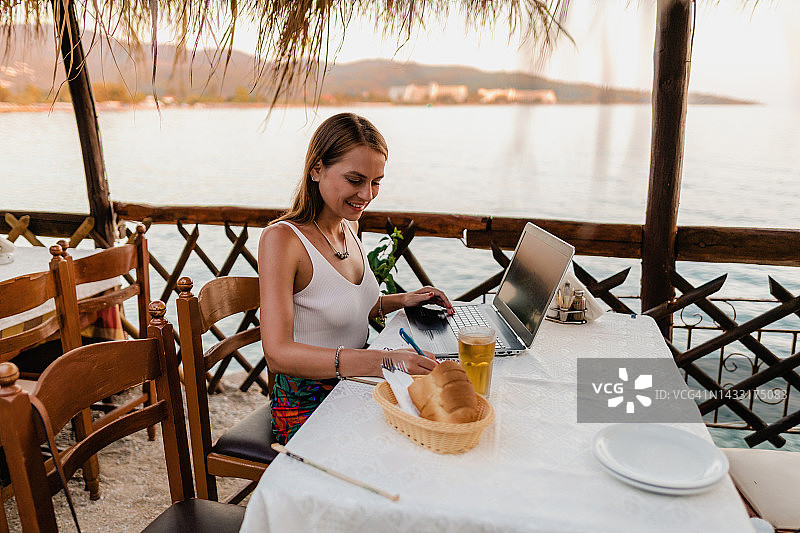 在希腊海边餐厅学习的年轻女人图片素材