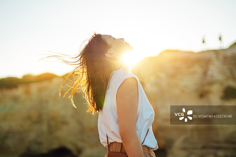 年轻女子在美丽的日落下闭着眼睛抬头图片素材