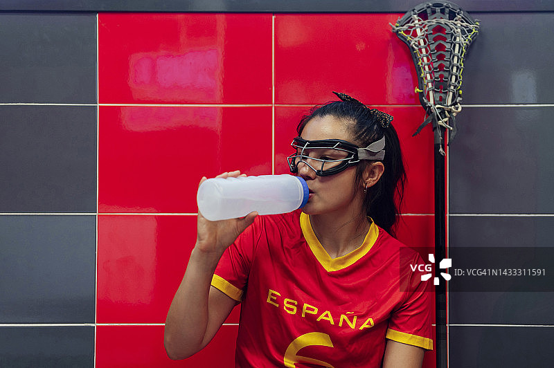 在更衣室喝水的戴防护眼镜的年轻女人图片素材