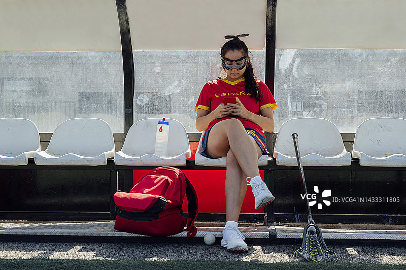 长曲棍球运动员在休息区长椅上使用手机图片素材