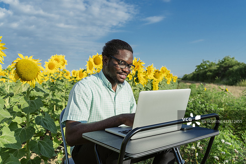 微笑的商人在向日葵田中用笔记本电脑图片素材