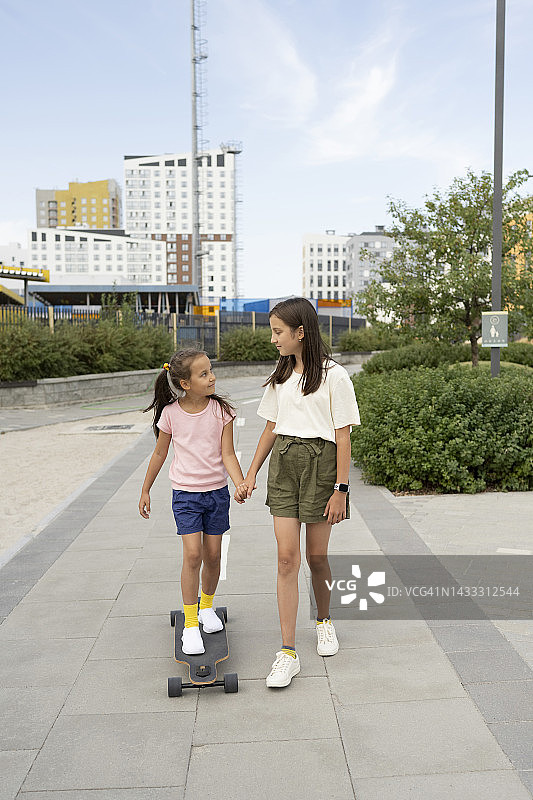 女孩牵着妹妹的手站在滑板上图片素材