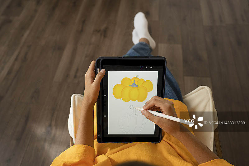 女孩在家用数位笔在平板电脑上绘制黄色南瓜图片素材