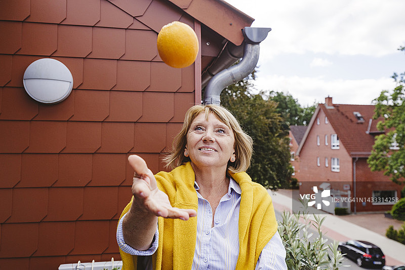 笑容满面的老年妇女在阳台上玩橙子图片素材