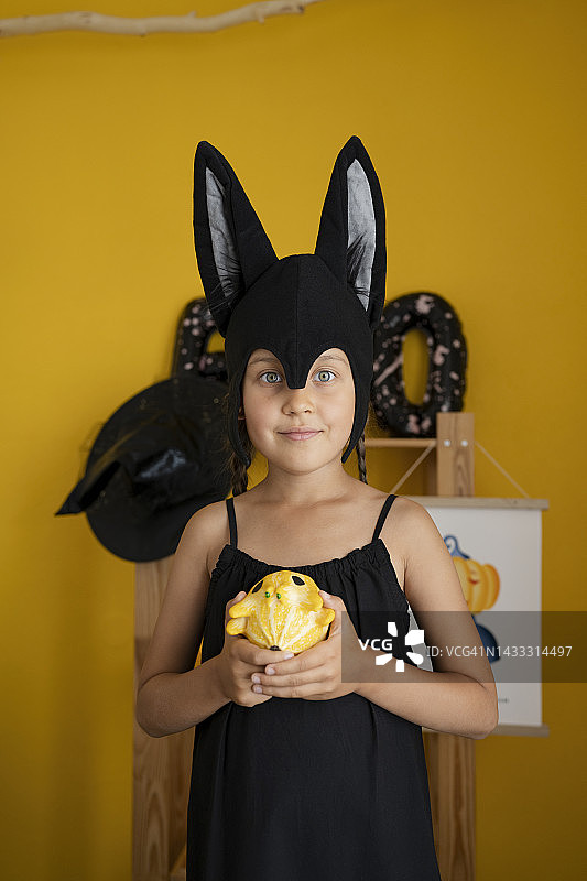 在黄色墙壁前手捧南瓜的微笑女孩图片素材