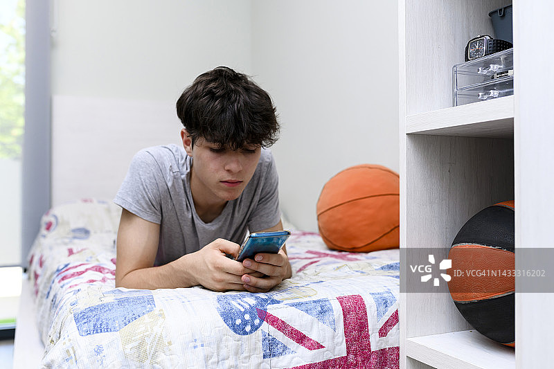 在卧室里使用智能手机的青少年男孩图片素材