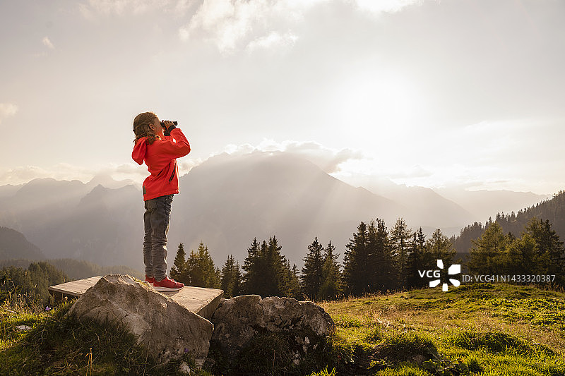 女孩站在长凳上用双筒望远镜观察图片素材