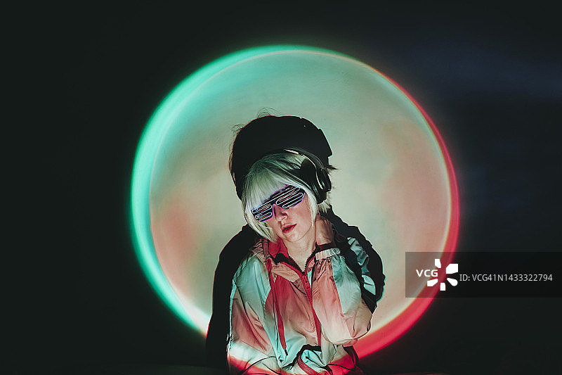 戴霓虹眼镜的女人站在聚光灯照亮的黑色背景前图片素材