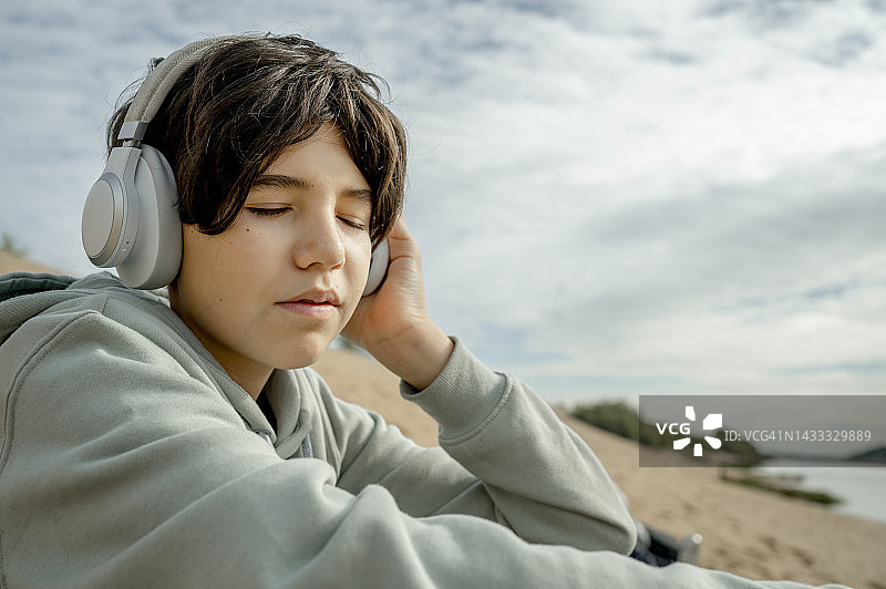在海滩上戴着无线耳机听音乐、闭着眼睛的男孩图片素材
