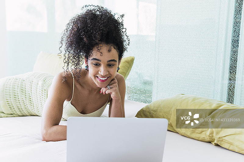 在家中床上使用笔记本电脑的卷发快乐女人图片素材