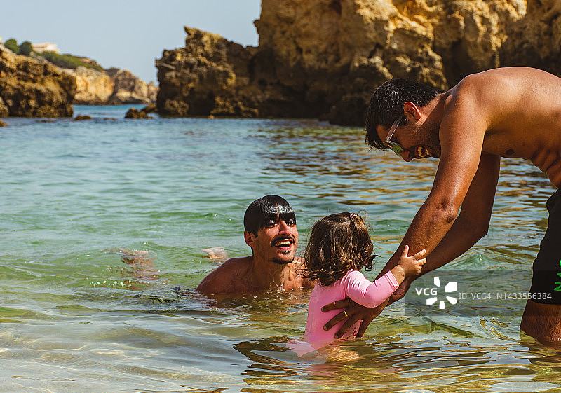 父亲和叔叔在海滩上与女婴互动图片素材