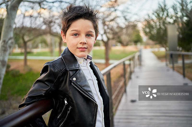穿着皮夹克靠在公园走道栏杆上的小男孩图片素材
