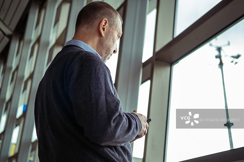 中年男人在窗边使用智能手机图片素材