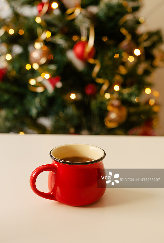 桌子上装有冬季热饮的红色杯子，背景是模糊的圣诞树和灯光图片素材