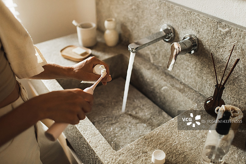 女人往电动牙刷上挤牙膏，个人卫生图片素材