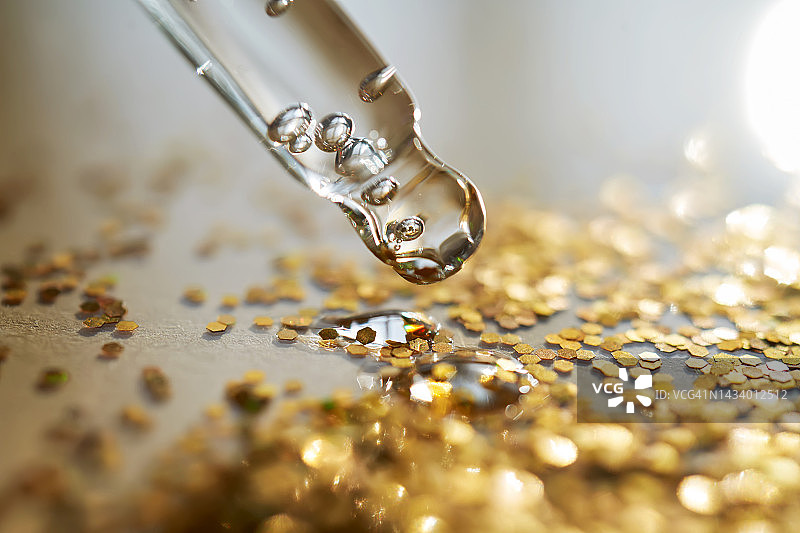 闪光金色亮片背景上的化妆品凝胶滴管图片素材