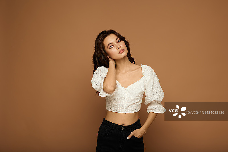 在米色背景工作室里，身穿白色衬衫的美丽年轻浪漫女孩的肖像图片素材