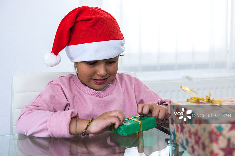 小女孩早上在客厅里戴着圣诞帽，打开圣诞礼物，圣诞节、礼物、情感、魔法和圣诞老人的概念图片素材