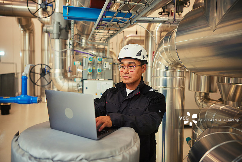 工程师在发电站管道旁使用笔记本电脑图片素材