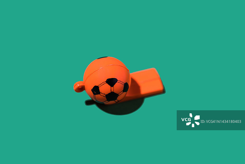 绿色背景上的足球造型橙色塑料口哨：世界杯、竞赛与规则图片素材
